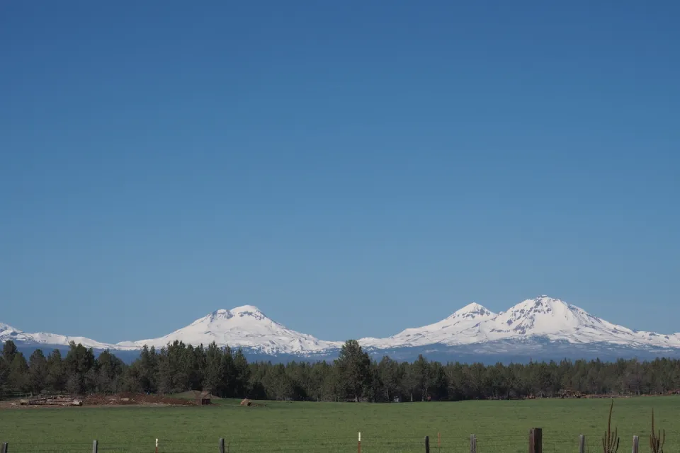 The Three Sisters, snow-covered mountains in Central Oregon, are visible in the distance beyond a farm.